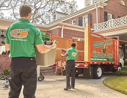 two college hunks moving items to a junk truck